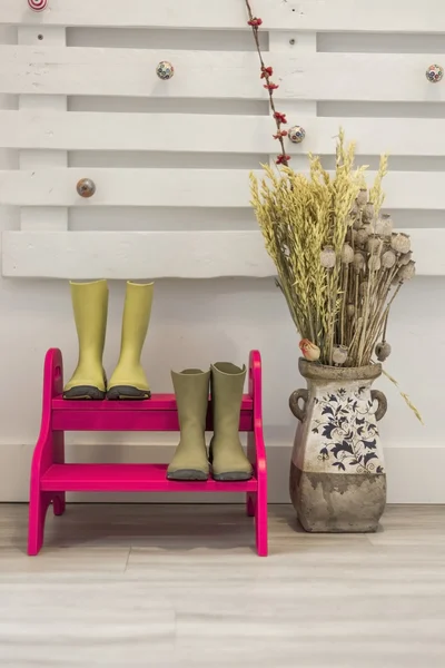 Green boots in a fuchsia steps ladder and a vase with dried flow