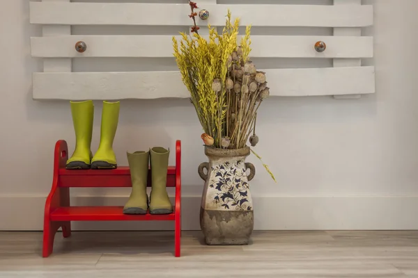 Green rain boots on red two steps ladder and a vase with dried f