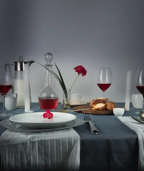 Still life. jug of milk, rose wine in glasses, bun, white candles on a blue tablecloth