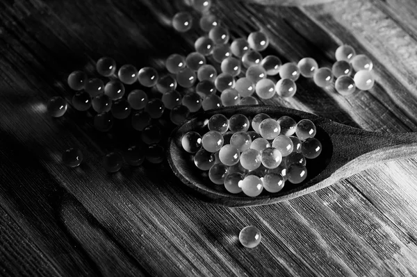 Round small fish oil capsules on wooden spoon scattered  a  surface. Black and white
