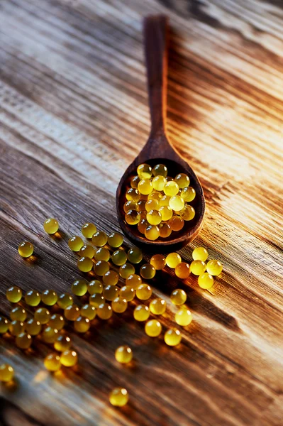 Round small fish oil capsules on wooden spoon scattered a surface