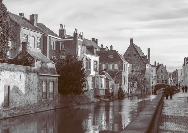 Bruges - February 2016, Belgium: View of typical street of medieval city of Bruges with traditional architecture, canal and walking people, sepia colors