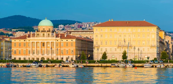 Trieste, Friuli Venezia Giulia region - July 2016, Italy: Front view of Trieste\'s Waterfront in golden hour, Palazzo Carciotti (tourist attraction) and other historical buildings reflected in water of Adriatic Sea