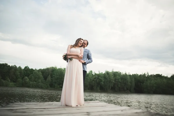 Charming bride, elegant groom on landscapes of mountains and sunset at lake. Gorgeous wedding couple