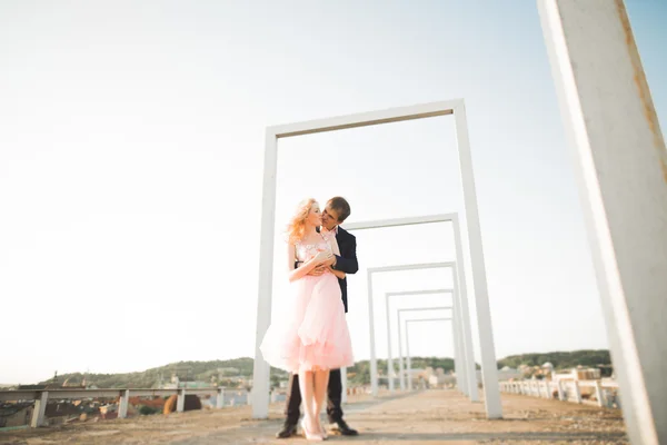 Young couple in love posing on roof with perfect city view holding hands and hugging . Beautiful sunset