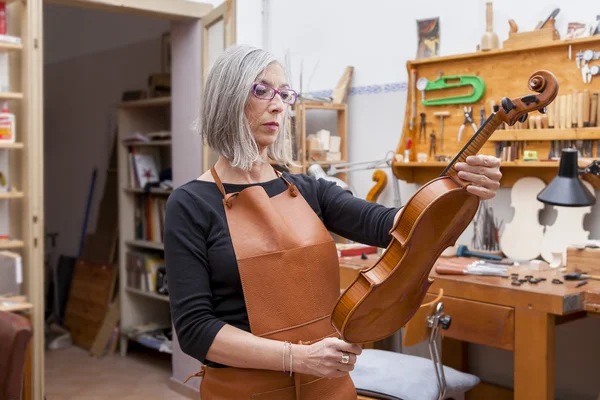 Portrait of female mature violin maker while testing the violins