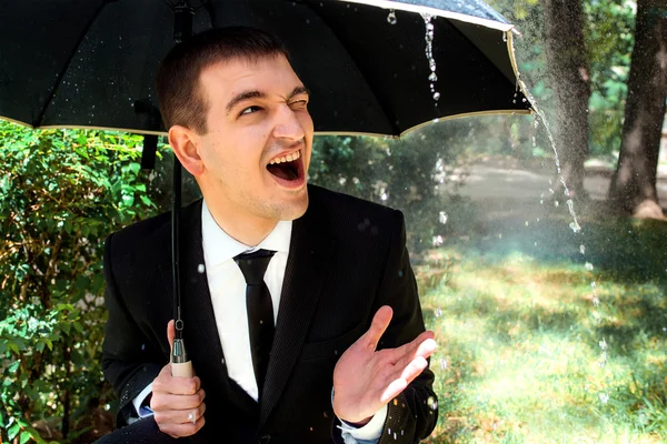 Young man in black suit in sunny raining day under umbrella