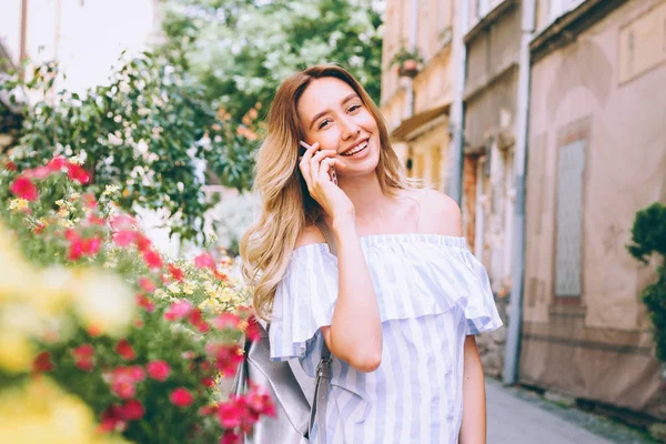 beautiful young blonde woman walking on the street and talking on a cell phone,the girl laughs and smiles,the perfect photo for mobile advertising  travel,shopping for magazines,photo -style lifestyle