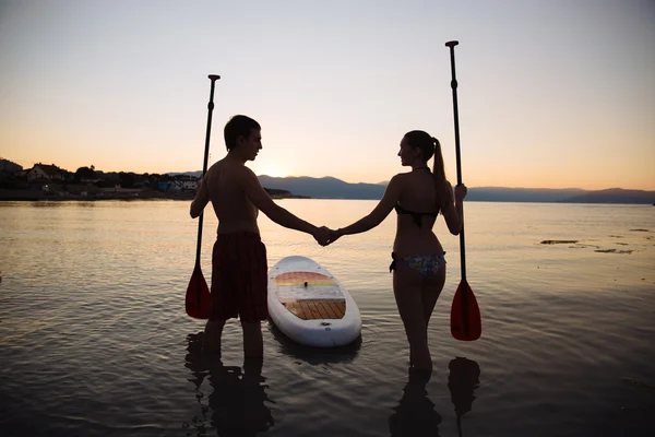 Silhouette of man, woman with sup surf and paddle at the ocean. Concept lifestyle, sport, love