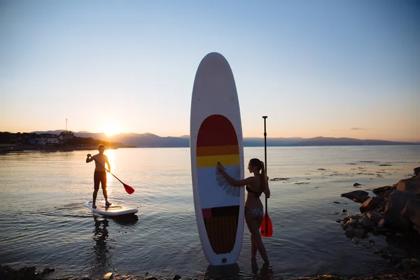 Silhouette of young sexy girl and man at background with sup surf  paddle in the sea. Sport concept