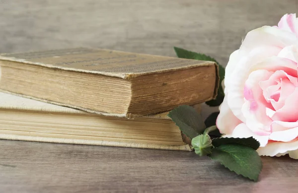 Old books and flower rose on a wooden background. Romantic floral frame background. Picture of a flowers lying on an antique book. Flowers on vintage wood background with romantic vintage background.