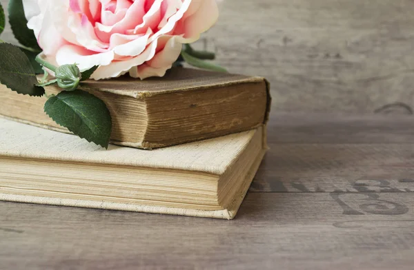 Old books and flower rose on a wooden background. Romantic floral frame background. Picture of a flowers lying on an antique book. Flowers on vintage wood background with romantic vintage background.