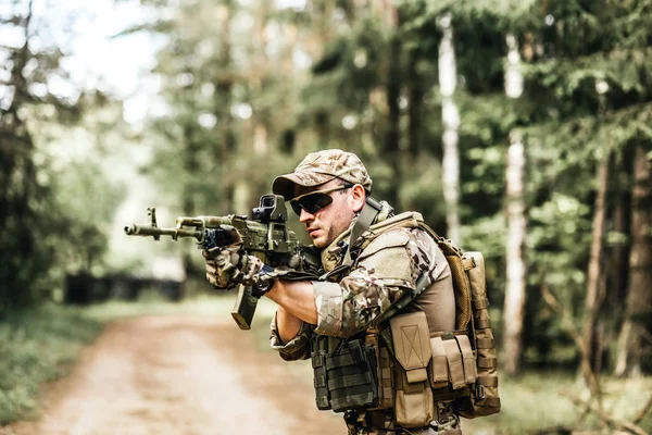 Armed young man in a zone of armed conflict soldier in uniform targeting with assault rifle outdoors