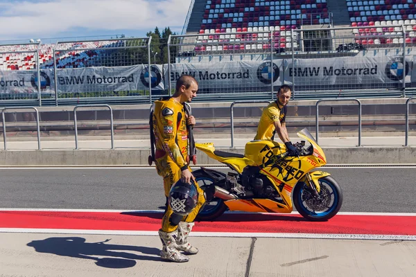 Rider yellow suit and helmet,  technical personnel to carry the bike around the pits after the race