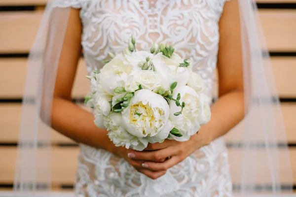 Wedding bouquet of white peonies in the hands of the bride