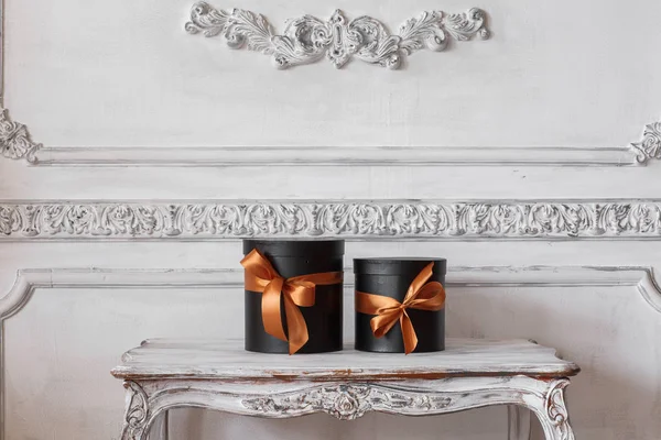 Wrapped gift black boxes with ribbons as Christmas presents on a table luxury white wall design bas-relief stucco mouldings roccoco elements