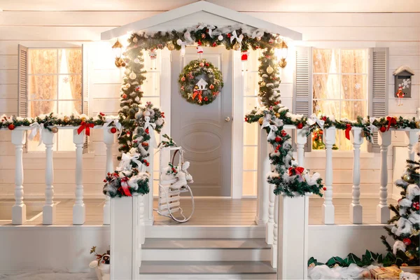 Green garlands of fir or pine branches with red and gold Christmas toys door on the veranda