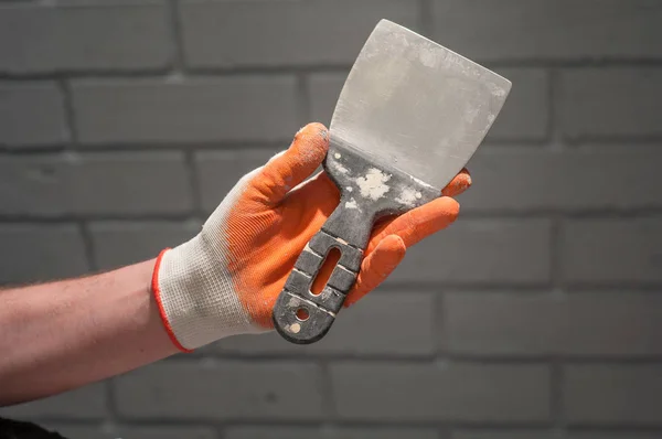 Male arm in rubber glove holding putty knife on the grey concrete textured even pattern linear brick wall background