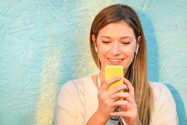 Happy girl connected to social media network and having fun with smartphone. Young woman smiling and typing on the phone against blue wooden background. Lifestyle concept of new trends and technology.