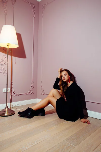 Portrait of a beautiful girl in a black dress sitting on the floor on a pink background