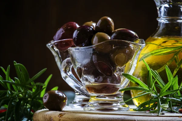 Black and green Greek olives in glass bowls with rosemary and oil in a jug