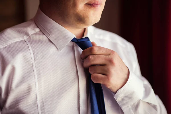 People, business, fashion and clothing concept - close up of man in shirt dressing up and adjusting tie on neck at home. Businessman putting on a tie. Man putting on necktie. Businessman getting dressed in the morning