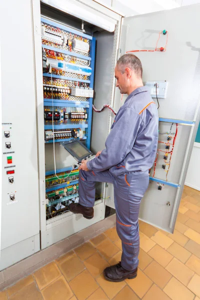 Electrician testing industrial machine, electrician builder engineer screwing equipment in fuse box, Male Electrician