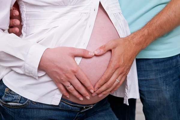 Belly of a pregnant woman, hands of mother and father holding a heart