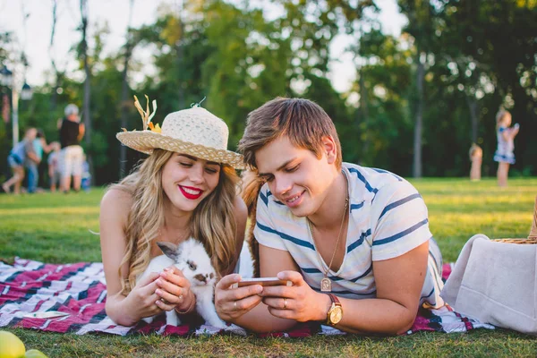 Young attractive couple resting in the park on the green lawn with dog and rabbit