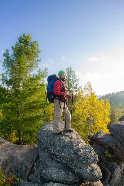 Man with backpack and trekking pole in bandana standing on a roc