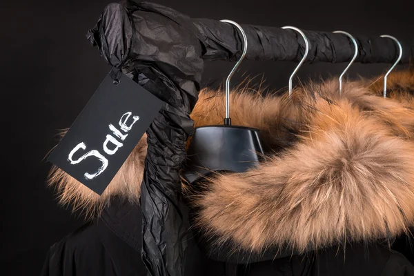Lot of black coats, jacket with fur on hood hanging  clothes rack.  background. Sale inscription.  friday.Close up.