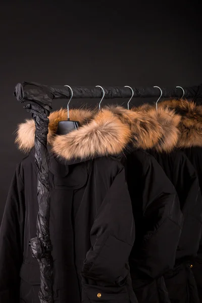 Lot of black coats, jacket with fur on hood hanging  clothes rack.  background.