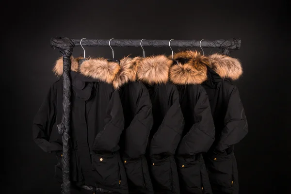 Lot of black coats, jacket with fur on hood hanging  clothes rack.  background.
