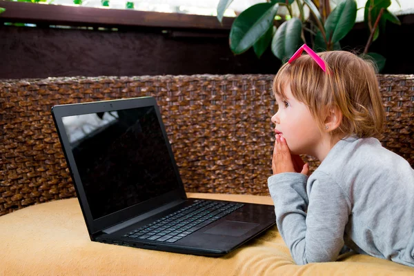 Little girl using laptop. Child in pink sunglasses, grey top lying at the sofa, playing, studying .