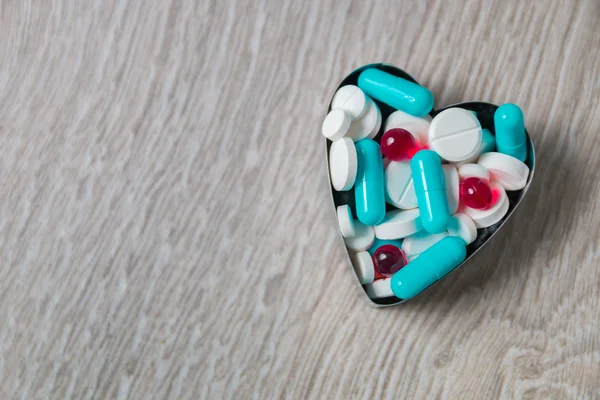 Heart from colorful medication and pills  above on grey wooden background. Copy space. Top view, frame. Painkillers, tablets, generic , drugs.