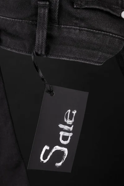 Sale sign hanging on  black  jeans with  background. Friday . Close up.