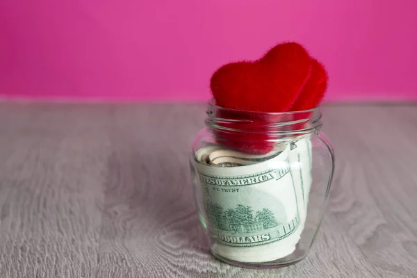 Money and red hearts. Dollars in open jar on grey wooden background.  Copy space. Love. Valentine day.