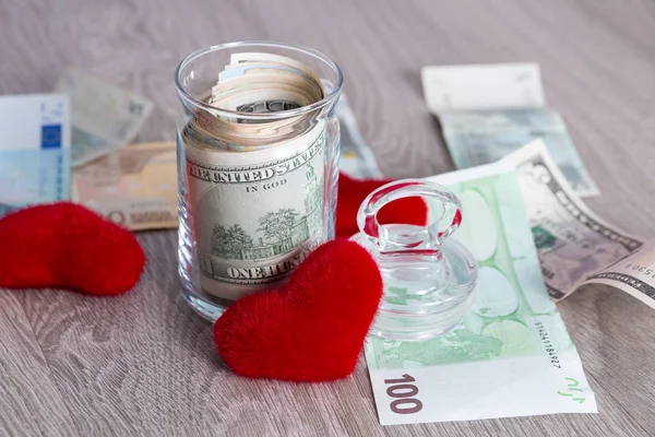 Money near red hearts. Dollars in open jar with euro on grey wooden background.  Copy space. Love. Valentine day.