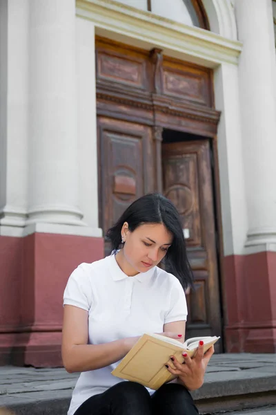 Woman is reading book. Girl with  in white polo, black pant and red shoes  sitting on stairs near university at campus  learning, studying. teenager  outdoors  open