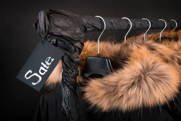 Black Friday. A lot of black coats, jacket with fur on hood hanging on clothes rack