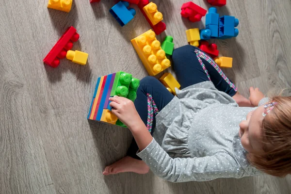 Unrecognizable Child girl having fun and build of bright plastic construction blocks. Toddler playing on the floor. Developing toys. Early learning. Top view.