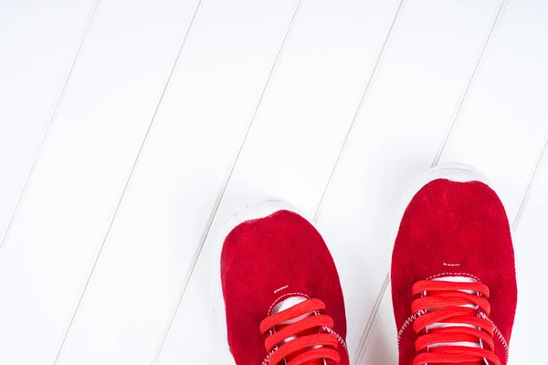 Red leather sneakers on a white wooden background.