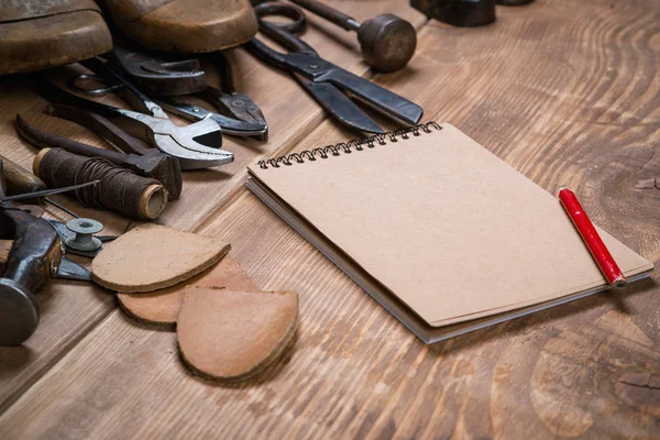 Set of tools, notebook, pencil for shoemaker on a wooden background.