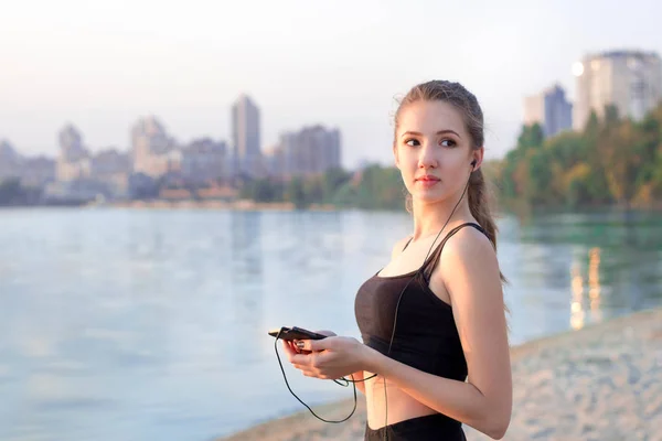 Fitness girl at lake listening to music on mobile phone