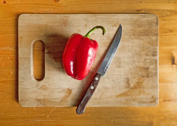 Red bell pepper and knife on wooden cutting board