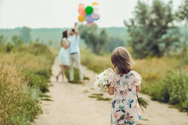 Daughter with a bouquet of camomiles walking on country road to meet his parents kissing balloons holding hands