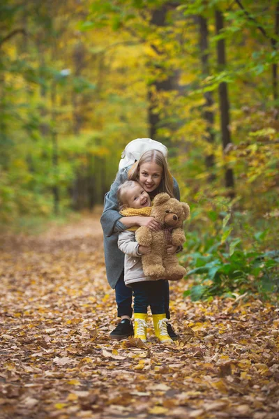 The mother, her daughter and toy Teddy bear posing and walking in autumn park