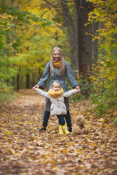 Mother and little daughter blonde walking posing in autumn park, yellow lives around