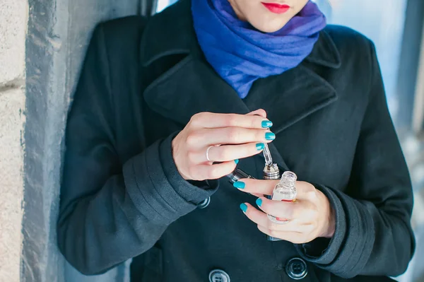 Portrait of young beautiful woman with white hair, in a black coat, a skirt and a black hat, smoking an electronic cigarette, runs vape juice electronic cigarette. He holds a mechanical mod with RDA.