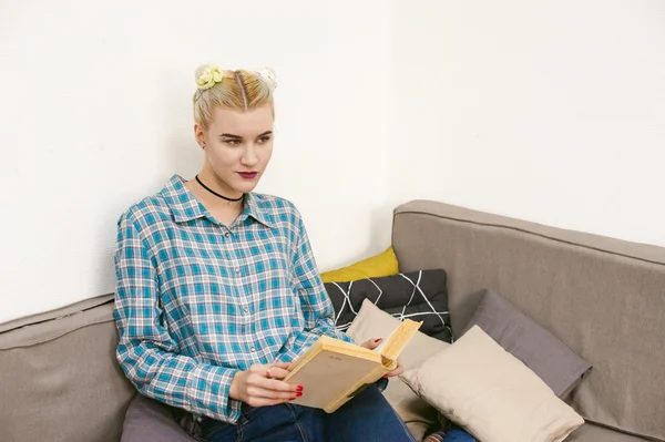 Young beautiful girl reading a book sitting on a sofa in the room
